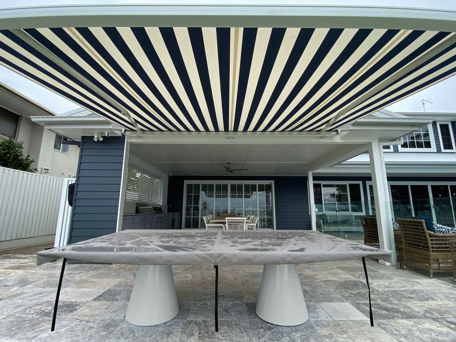 A navy and white striped folding arm awning shading a tiled outdoor dining area.